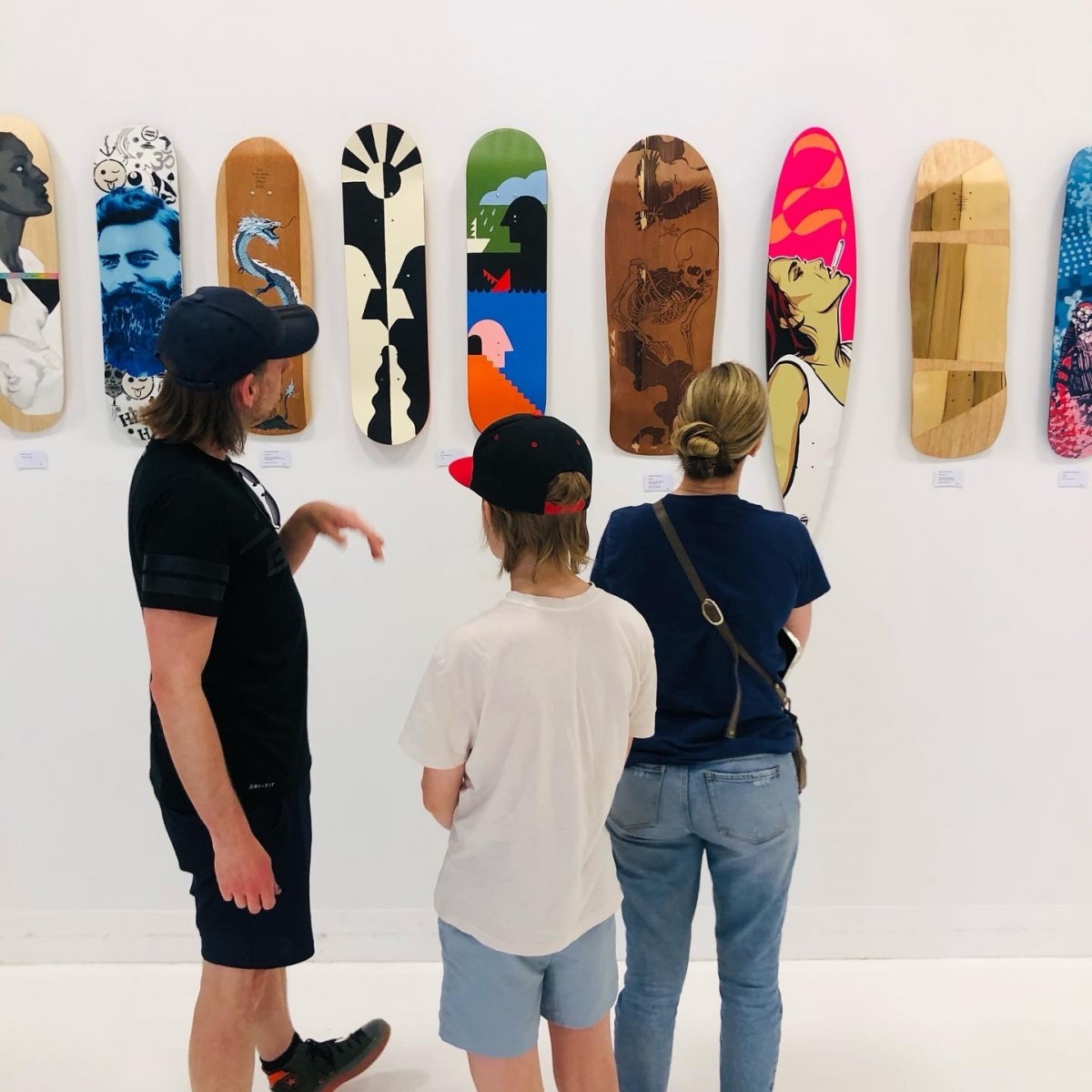 2 adults and child looking at art on skateboards