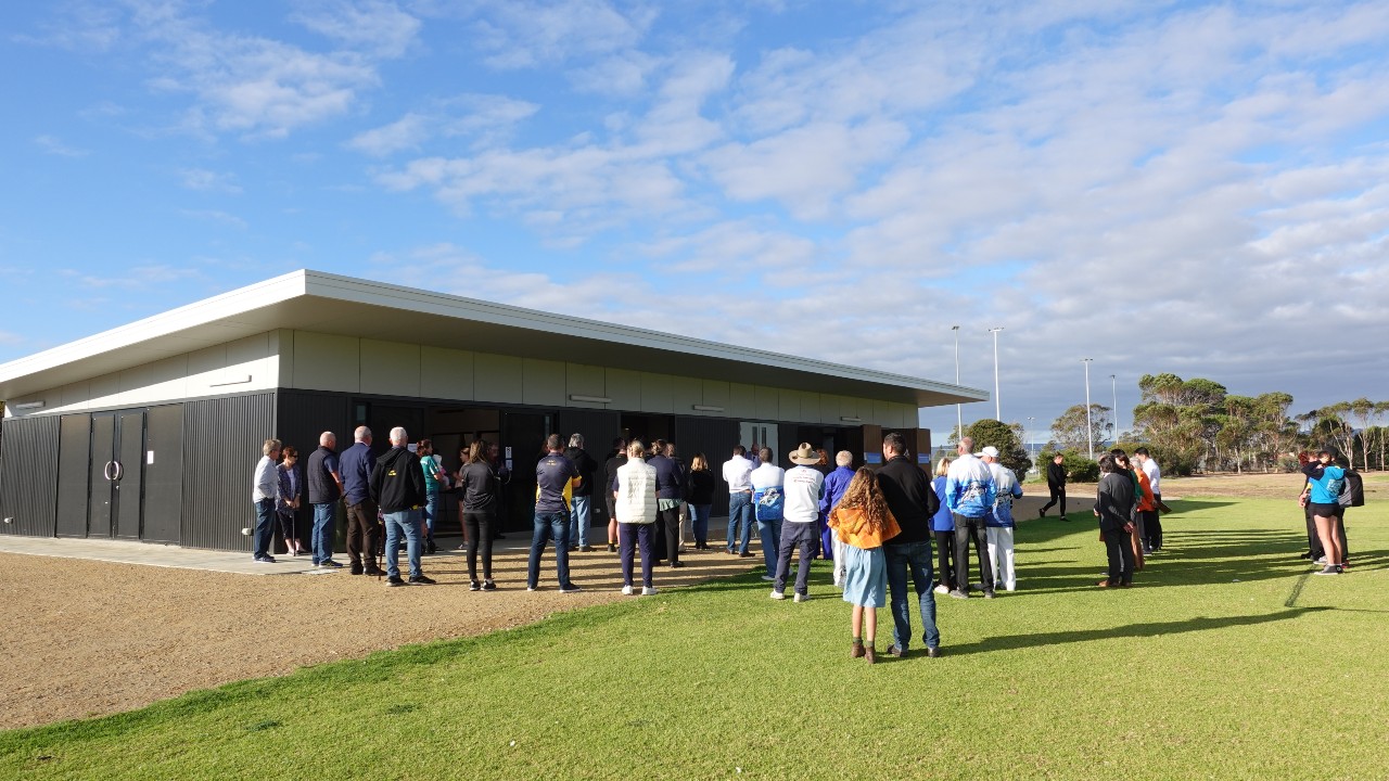 People gathered outside new sporting building on sunny day.