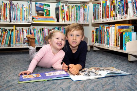 2 smiling children at the library reading books
